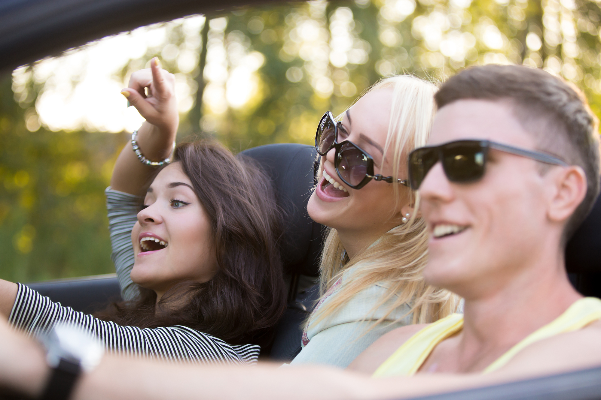 Group of three carefree cheerful friends on vacations, traveling in convertible on summer day, having fun together
