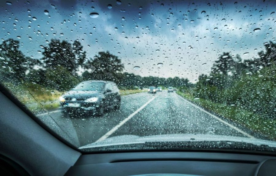 Vista desde el interior de un auto conduciendo bajo la lluvia antes de salir a la ruta, con parabrisas mojado y tráfico en carretera