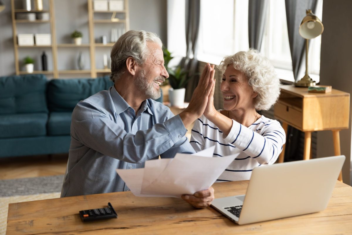 Pareja de adultos mayores celebrando resultados financieros tras revisar documentación vinculada a un seguro de retiro.