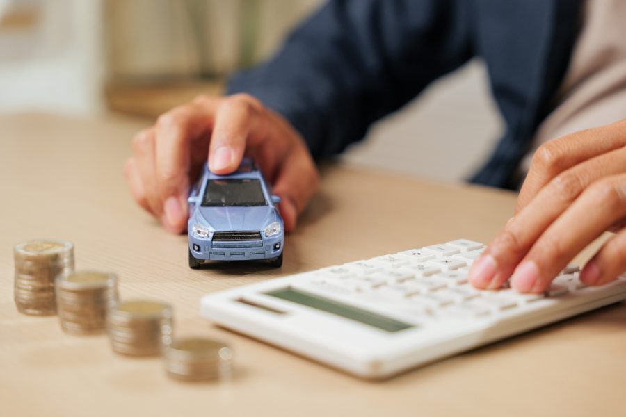Mano sosteniendo un auto en miniatura junto a una calculadora, ilustrando el análisis del patentamiento del auto y sus costos en Argentina.