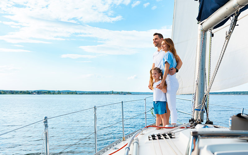 Familia disfrutando sobre la proa de un velero en navegación, representando la seguridad que brinda un seguro para lanchas y veleros.