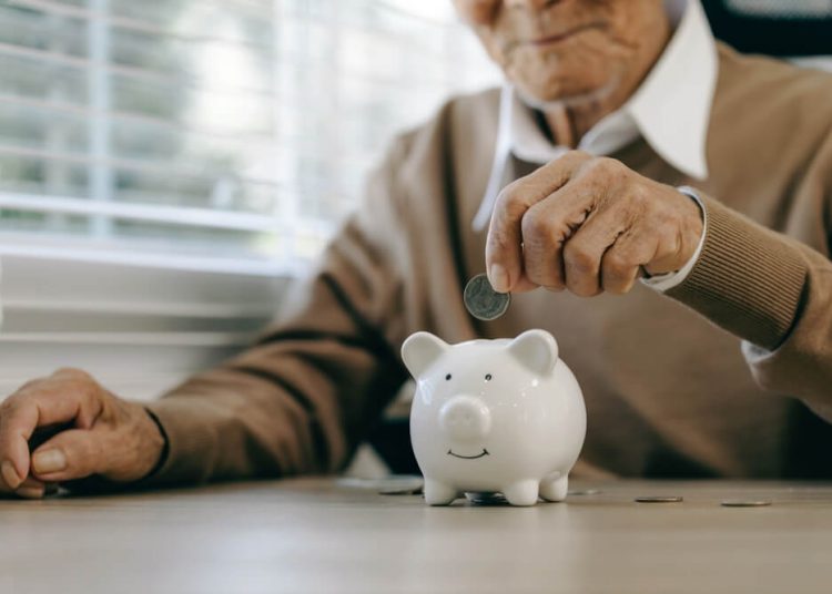 Persona mayor colocando una moneda en una alcancía, representando el ahorro a largo plazo asociado a un seguro de retiro.