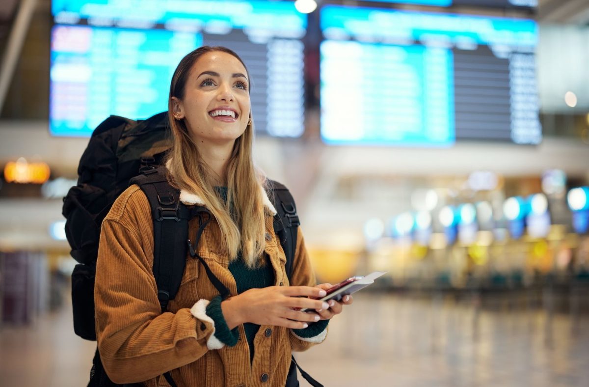 Mujer en aeropuerto con mochila y boarding pass buscando pasajes a Brasil en temporada baja.