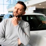 Hombre analizando vehículo en concesionaria para estimar su valor fiscal antes de comprar.