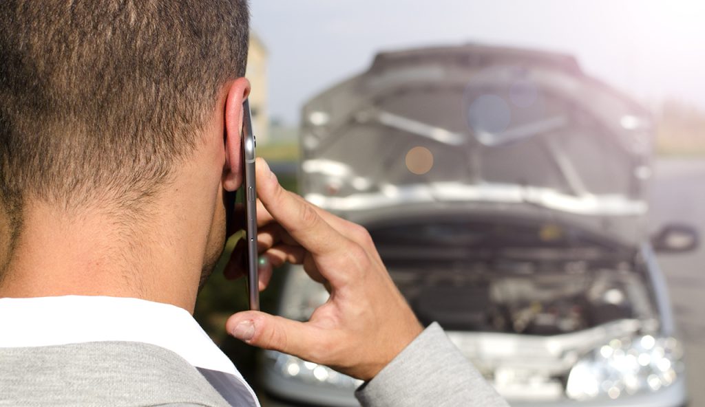 Conductor llamando por teléfono junto a vehículo con capó abierto en la vía pública, situación que resalta la importancia de comparar seguros de auto en Argentina.