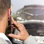 Conductor llamando por teléfono junto a vehículo con capó abierto en la vía pública, situación que resalta la importancia de comparar seguros de auto en Argentina.