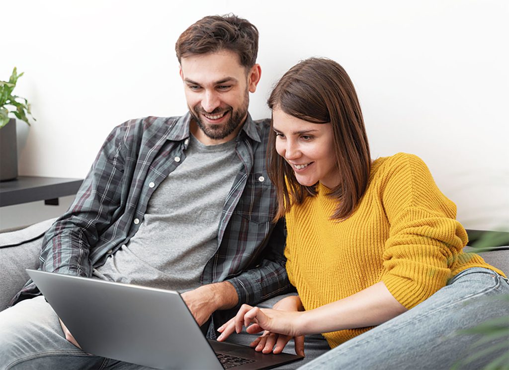 Pareja comparando precios de pasajes a Brasil en una computadora portátil desde su hogar.