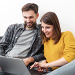 Pareja comparando precios de pasajes a Brasil en una computadora portátil desde su hogar.